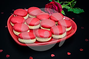 Red macaroon on black background with red roses heart shaped plate photo