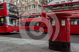 Red mailbox in London with double decker bus passing by