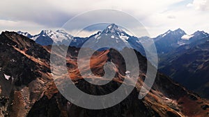 Red majestic rocks dusted with snow high in the mountains. Flying near high peaks and mountain tops at sunset. Aerial