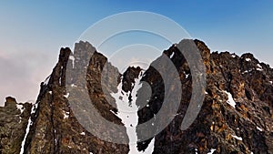 Red majestic rocks dusted with snow high in the mountains. Flying near high peaks and mountain tops at sunset. Aerial