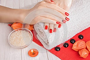 Red manicure with dekor and towel on white wooden table.