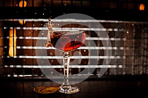 Red martini cocktail splashing into glass on dark background