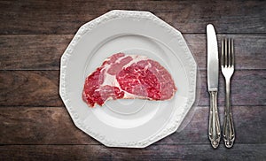 Red meat / raw steak on plate on wooden background with knife and fork