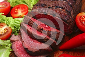 Red meat served on wooden plate with vegetables