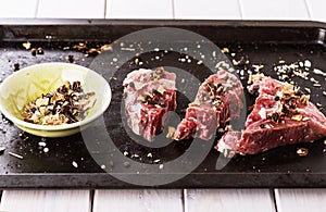 Red meat and spices on a rustic metal tray