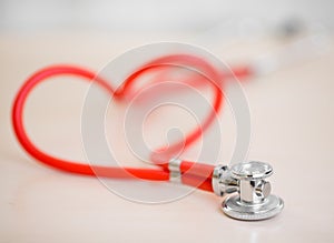 Red medical stethoscope in shape of heart on table