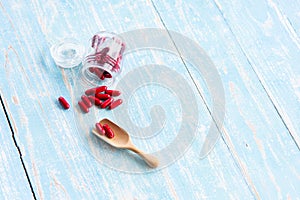 Red medicines in the glass bottles on the wooden spoon and blue table.