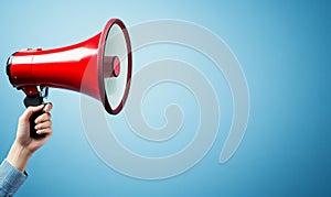 A red megaphone held by a hand against a blue background with copy space