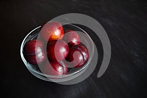 Red mellow plums in transparent glass bowl on dark background. Close-up.