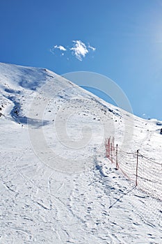 Red mesh fence marking the dangerous area and the border of the route. Empty piste at ski resort, mountain slope