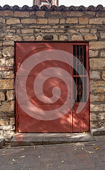 Red metal door with lattice closed on chain with lock in old stone wall. Vertical photo