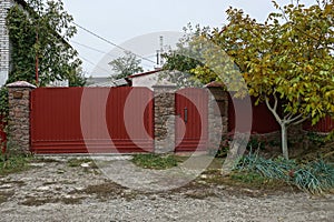 Red metal gate and door with part of the fence in the vegetation outside