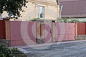 Red metal gate and door on the wall of a fence made of iron and brown bricks