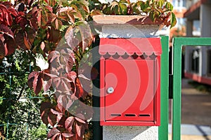 Red metal letter box on stone column near gate outdoors