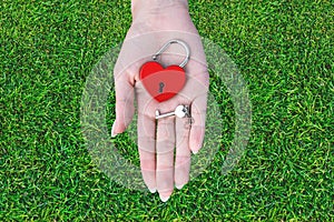 Red metal lock of love and a key in the shape of a heart on a female palm on a background of green grass. Love