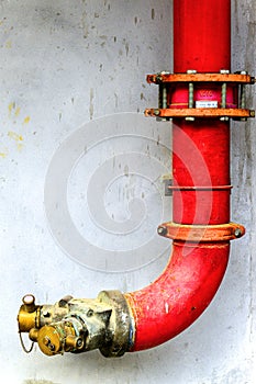 Red metal pipe extinguishing water on concrete wall. Emergency fire valve or Y shape hose tube in the building. Safety equipment a