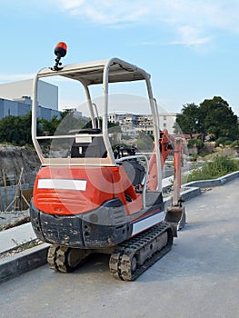 Red mini excavator on tracks for small construction works in hard-to-reach places or on narrow city streets