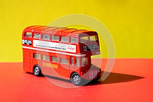 A red miniature toy bus, London Route Master bus. against a bright red and yellow background with black shadows