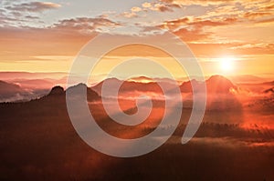 Red misty daybreak. Foggy autumn morning in a beautiful hills. Peaks of hills are sticking out from rich colorful clouds.