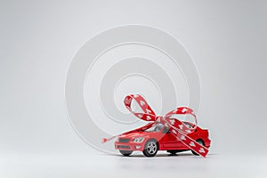 Red model car with bow on a white background. Car as gift, surprise.
