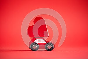 Red model of car delivering red paper heart on red background. Creative greeting card for Saint Valentine day