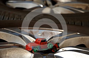 Red model car pickup with green wheels painted by small children while their car game lies on real silver car wheels