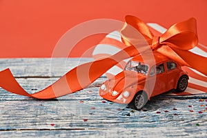 red model of a retro car on a blue wooden surface with a red ribbon bow on the roof, red background