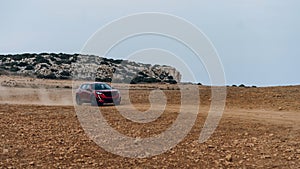 Red modern car driving on dirt road of Cape Greco, Cyprus