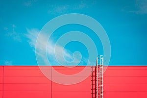 A red modern facade of an industrial building, warehouse or shopping center with a long metal staircase against the blue sky.