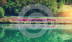 Red modern high speed train and river in mountains at sunrise