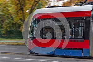 Red modern public electronic railway tram on street with forest