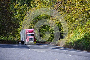 Red modern semi truck with trailer going up hill in autumn trees