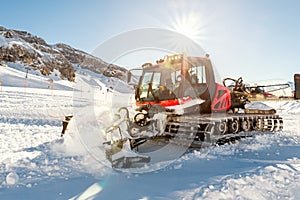 Red modern snowcat ratrack with snowplow snow grooming machine preparing ski slope piste hill at alpine skiing winter