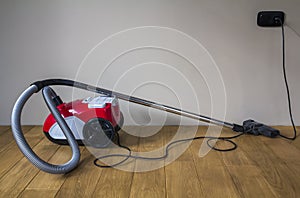 Red modern vacuum cleaner with black electric cable on wooden pa