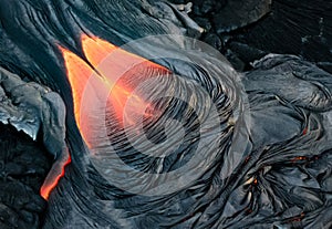 Red molten lava slowly moves across land, solidifying as it cool
