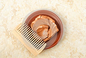 Red moroccan bentonite clay in a small ceramic bowl and wooden hairbrush comb. Diy facial or hair mask, body wrap recipe.