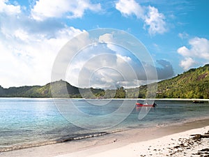 Red motor boat anchored off a sunny Seychelles beach with distant clouds and shoreline