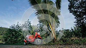 The red motorbike on forest road trail trip. One scooter, near tropical palm tree. Asia Thailand ride tourism. Single