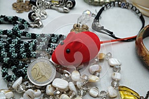 A red mouse, in the midst of costume jewelry, gnaws a two euro coin. Saving erosion concept