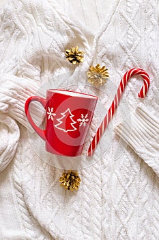 Red mug and candy cane on white knitted sweater. Christmas mood