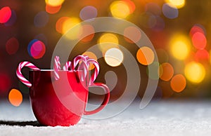 Red mug with candy canes in snow with defocussed fairy lights, bokeh in the background, Festive Christmas background