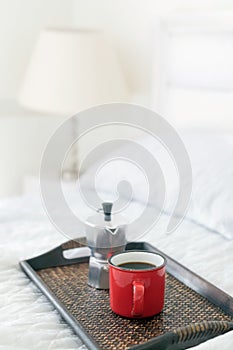 Red mug of coffee with steel coffee percolator on bed