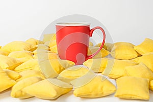 Red mug of coffee is among the yellow pillows
