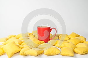 Red mug of coffee is among the yellow pillows