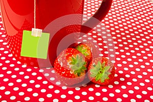 Red mug cup with teabag and strawberries over red background like fruit tea concept