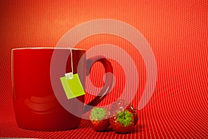 Red mug cup with teabag and strawberries over red background like fruit tea concept