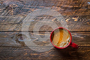 Red mug with freshly brewed coffee with appetizing crema on aged wood kitchen table. Cozy winter fall holiday atmosphere