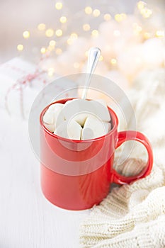 Red Mug with Hot Chocolate Cocoa Drink and Marshmallows Spoon. Glittering Sparkling Garland Lights. Knitted Sweater Gift Box