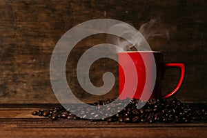 red mug with steam on a pile of fresh roasted coffee beans over wooden table