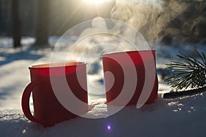 Red mugs with a hot drink soar in the cold, mugs in the snow on a Sunny frosty day, picnic in the winter